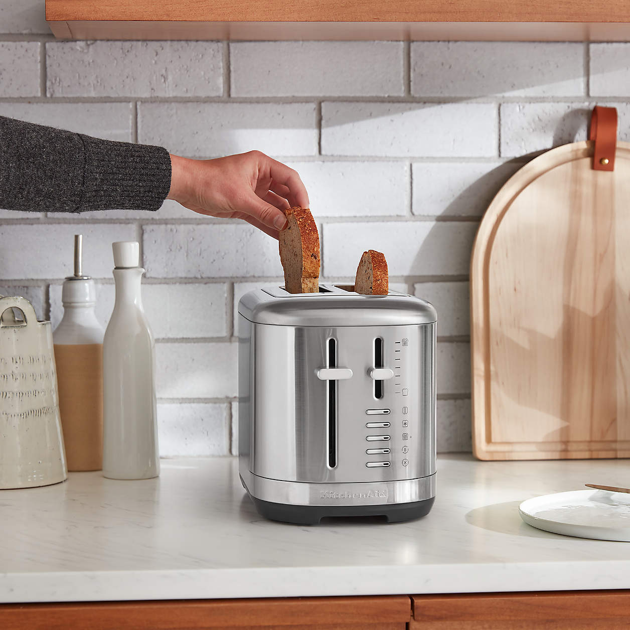 Hand placing toast into a sleek silver toaster on a kitchen counter.
