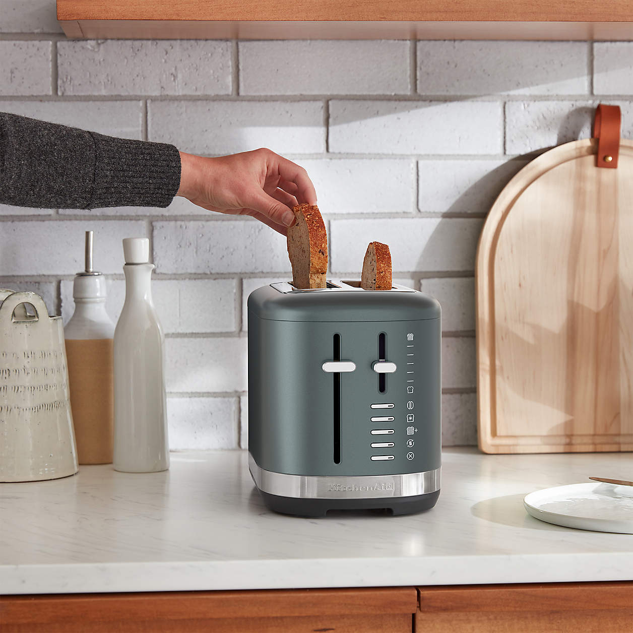 A hand placing toast into a modern grey toaster on a kitchen counter.