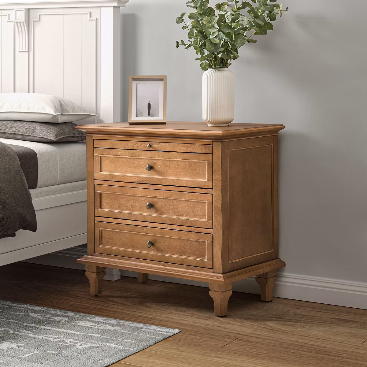 Wooden nightstand with three drawers in a cozy bedroom corner.